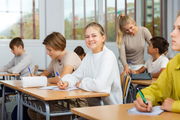 Fototapeta premium Teen boys and girls sitting at desk in classroom full of pupils during lesson