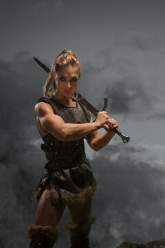 Fantasy woman warrior in laether armor stained with blood and mud, holding sword. Cosplayer historical viking