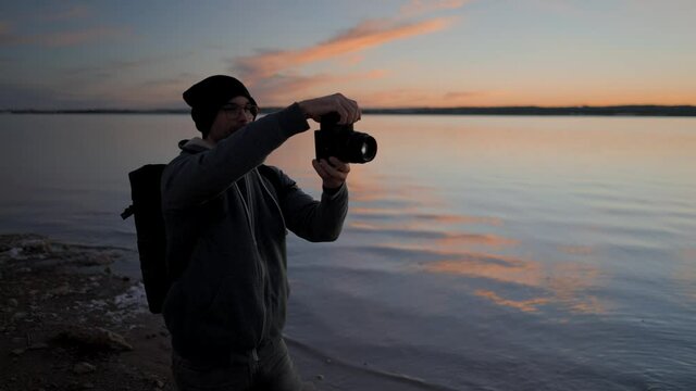 Young man photographer taking pictures with a professional camera by the Torrevieja Pink lake at sunset 