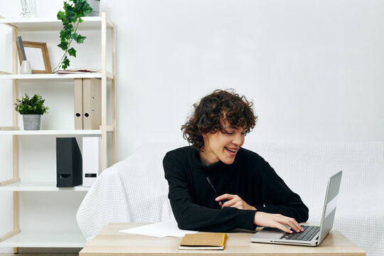 curly guy sitting on the couch at the table in front of a laptop Lifestyle technology