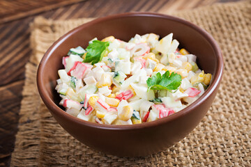 Salad with corn and crab sticks in bowl on wooden table. Traditional Russian cuisine.