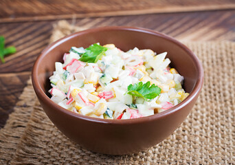 Salad with corn and crab sticks in bowl on wooden table. Traditional Russian cuisine. © timolina