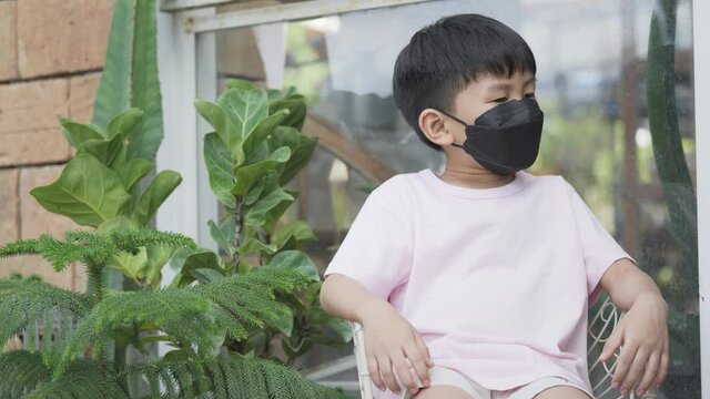 Asian boy with hyperactive kid syndrome or ADHD. A 5 years old kid keep moving his body while waiting on the chair with face mask.