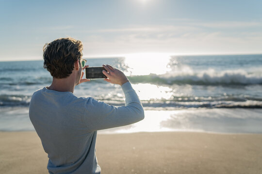Man using a mobile phone on the beach for taking pictures