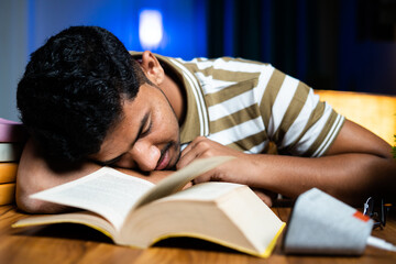 Young student sleeping on table due to taired of reading for examination at home - concept of hard working, lazyiness and late night studying