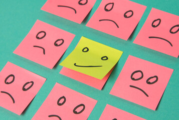 Post it sheets of different colours with sad emotions drawn on them and a happy face in te middle