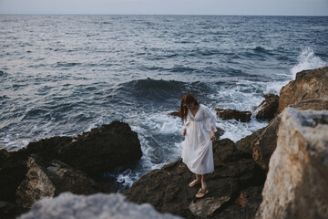 Fototapeta na wymiar a woman in a wedding dress stands by the ocean on a cliff