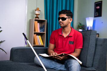 Blind young man reading by touching book at home - concept of education, self development and...