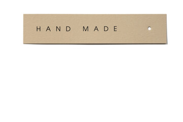 Clothes tag of rectangle shape positioned horizontally on white background, with small hole in right side with inscription on it indicating that product hand made. 