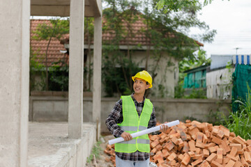 engineer concept The young engineer wearing black plaid shirt covered with light green shirt and a yellow safety helmet pointing at the second floor of the building