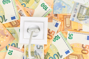 White socket with plug on Euro banknotes background. Increasing cost of electricity, expensive energy concept