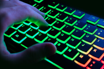 Professional online gamer hand fingers keyboard in neon color. Close-up.