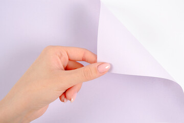 A woman's hand turns over or bends the corner of a blank sheet of blue-purple color