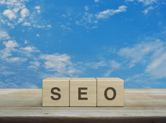 SEO letter on block cubes on wooden table over blue sky with white clouds, Technology search engine optimization ranking concept