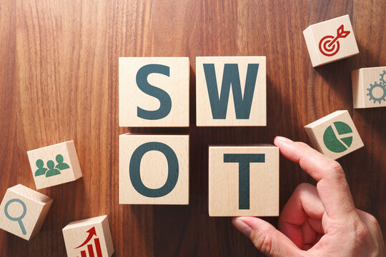 The word "SWOT". Concept image of SWOT analysis in business management. Putting wood cubes with alphabets and icons. Top view of wood table.