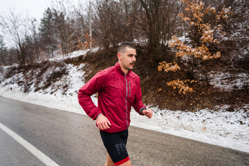 One adult caucasian man running in winter day male athlete runner training on the open road in nature with snow falling around health and fitness concept real people copy space side view half length