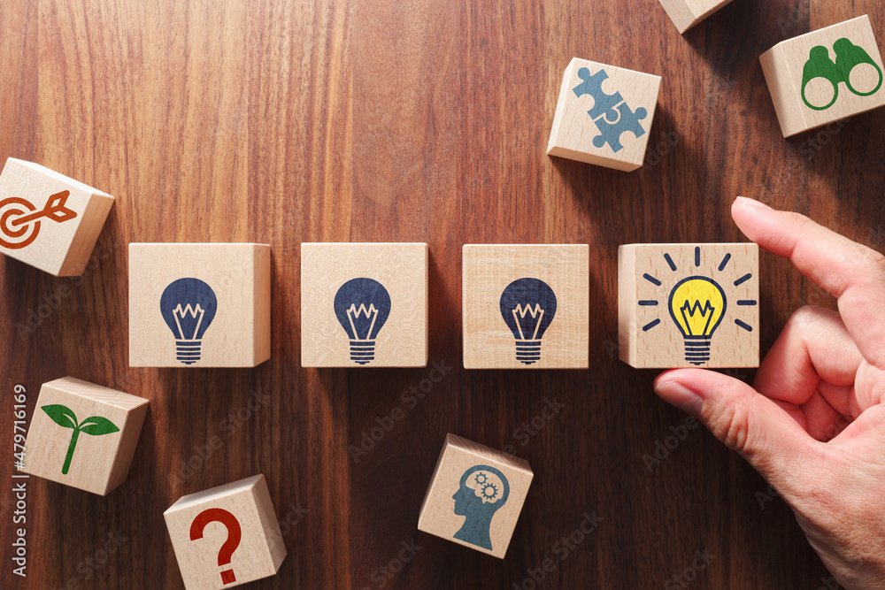 Poster Turning on light bulb. Idea and trial and error concept. Putting wood cubes with icons on table. Top view of wood table.