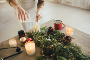 Woman making candle of soy wax, using wooden stick.