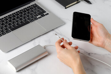 Women's hands with a phone and a powerbank. Charging the phone with a cable. Laptop and notebook...