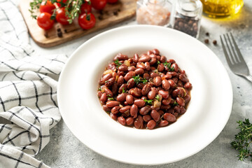 Stewed red beans with onion and thyme in tomato sauce in a white plate on the kitchen table closeup
