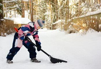 A child cleans up snow with a shovel in winter 