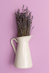 dried lavender flower in a white jug on a purple background