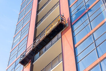 Suspended elevator on a high residential building under construction, decoration of the facade and windows. © aapsky