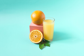 Fresh orange juice in a transparent glass with a decor of oranges and green leaves on a light green background.