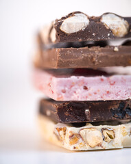 Pieces of different chocolate isolated on white background. Trendy, new type ruby, white, milk and dark chocolate sliced with nuts and dried fruits. Yummy chocolate pieces on white background
