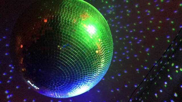 A close up shot of a shiny disco ball slowly spinning and reflecting multi-colored club lights during a dance party inside of a dark, underground nightclub in downtown Atlanta.