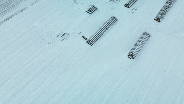 Flying over a snowy field. Straw bales are stacked. Traces of agricultural tillage are visible under the snow. Aerial photography.