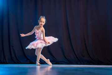little girl ballerina is dancing on stage in white tutu on pointe shoes classic variation.
