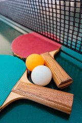 Table tennis rackets and ping-pong balls on green table surface with net
