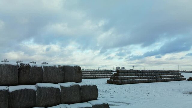Flying over a snowy field. Straw bales are stacked. Traces of agricultural tillage are visible under the snow. Aerial photography.