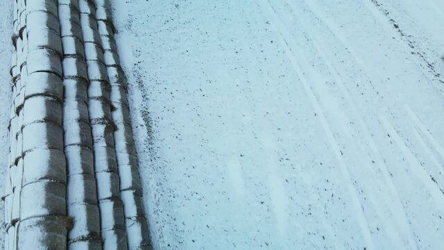 Flying over a snowy field. Straw bales are stacked. Traces of agricultural tillage are visible under the snow. Aerial photography.