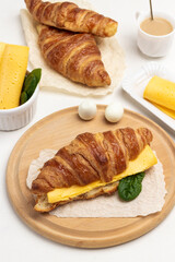 Breakfast products. Croissant with cheese and greens, two eggs on board.