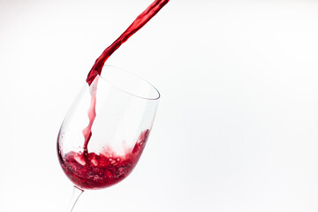 Red wine pouring in the glass on white background close up. Splashes and  drops of wine