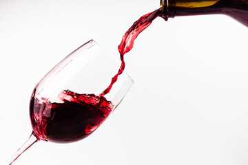 Red wine pouring in the glass on white background. Wine glass, bottle and splashes of red wine