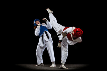 Dynamic portrait of two young women, taekwondo athletes training together isolated over dark background. Concept of sport, skills © master1305