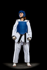 Portrait of young girl, taekwondo practitioner posing isolated over dark background. Concept of sport, skills