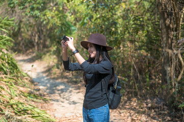 Naklejka premium Young woman trekker taking photos of nature with camera in the woods, holidays and traveling concept.