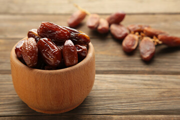 Wooden bowl of dried dates on grey wooden background.