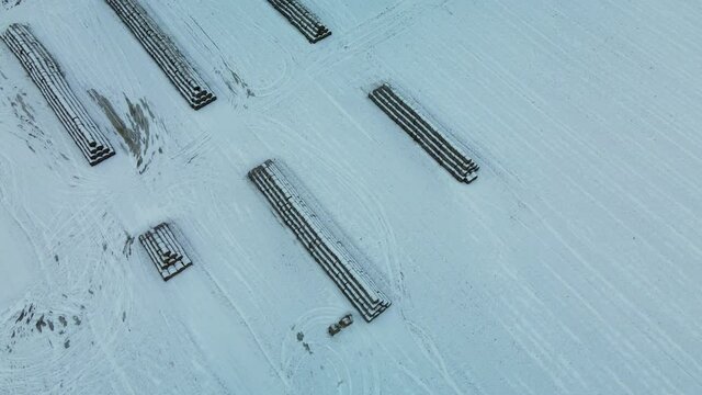 Flying over a snowy field. Straw bales are stacked. Traces of agricultural tillage are visible under the snow. Aerial photography.