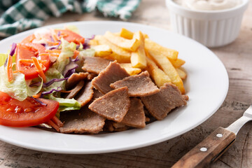 Plate of kebab, vegetables and french fries on wooden table	