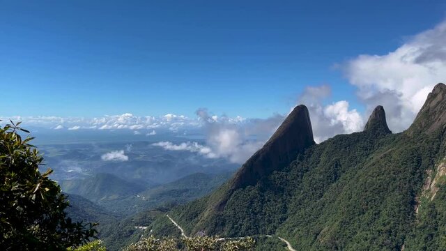 Lush Brazil mountainous Atlantic forest landscape of mountain range Serra dos Orgaos in Teresopolis, Rio de Janeiro with Dedo de Deus, Gods finger, peak in the middle against a blue sky with clouds