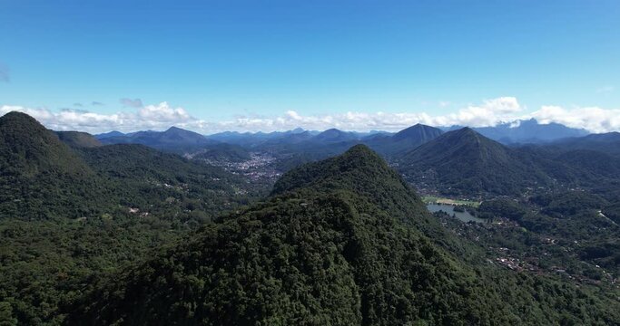 Aerial approach of Postcard trail viewpoint on mountain ridge part of Serra dos Orgaos with Teresopolis in the background against a blue sky.