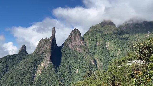 Panoramic landscape of mountain range Serra dos Orgaos in Teresopolis with Dedo de Deus, Gods finger, peak in the middle and clouds behind. 60fps in normal speed.