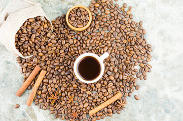 scattered coffee beans on a marble table with a cup of aromatic coffee. Cinnamon sticks and star anise to improve the taste of coffee. top view.
