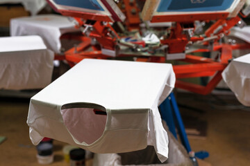 a white t-shirt on wooden shelve of the print screening apparatus. serigraphy production. printing images on t-shirts