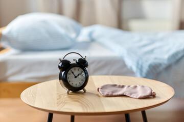bedtime and morning concept - close up of alarm clock and eye sleeping mask on night table at home